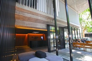 Zona de recepción de un hotel con diseño moderno, que incluye un mostrador de recepción, un área de estar y puertas de vidrio que dan a la calle.