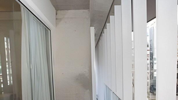 Un pasillo estrecho con suelo de madera, paredes blancas y un vidrio con cortinas.