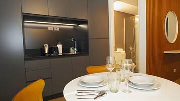 Een moderne eethoek met een ronde tafel gedekt voor vier personen, compleet met witte borden, glazen en bestek. Een inbouwkast boven de tafel bevat een koffieapparaat en andere voorzieningen.