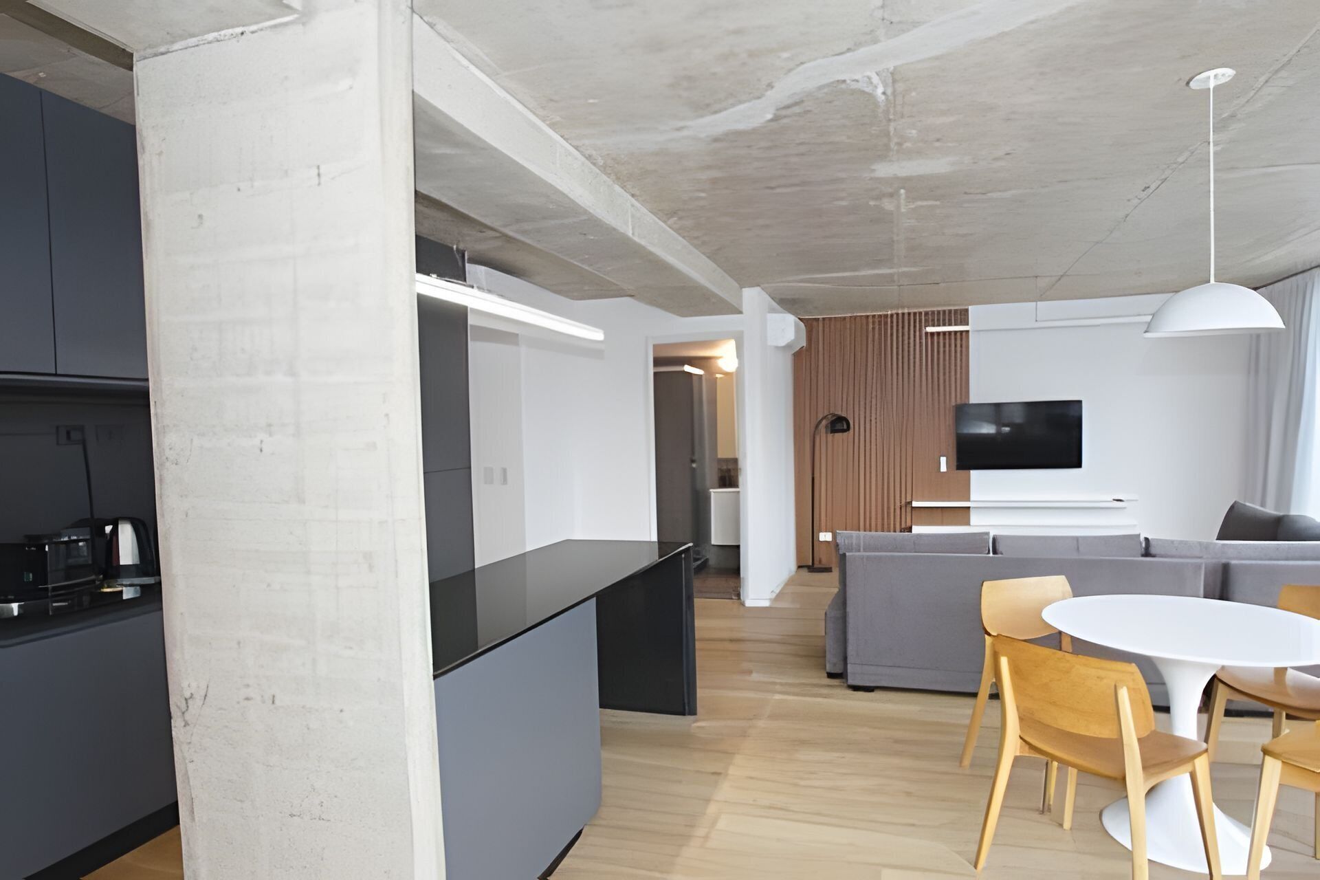 Une cuisine moderne avec un îlot central, un coin repas avec une table ronde et des chaises, un canapé gris et un téléviseur à écran plat fixé au mur.