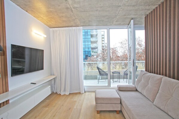 Una sala moderna con un televisor de pantalla plana, un sofá beige y un ventanal corredero que da a un balcón exterior.