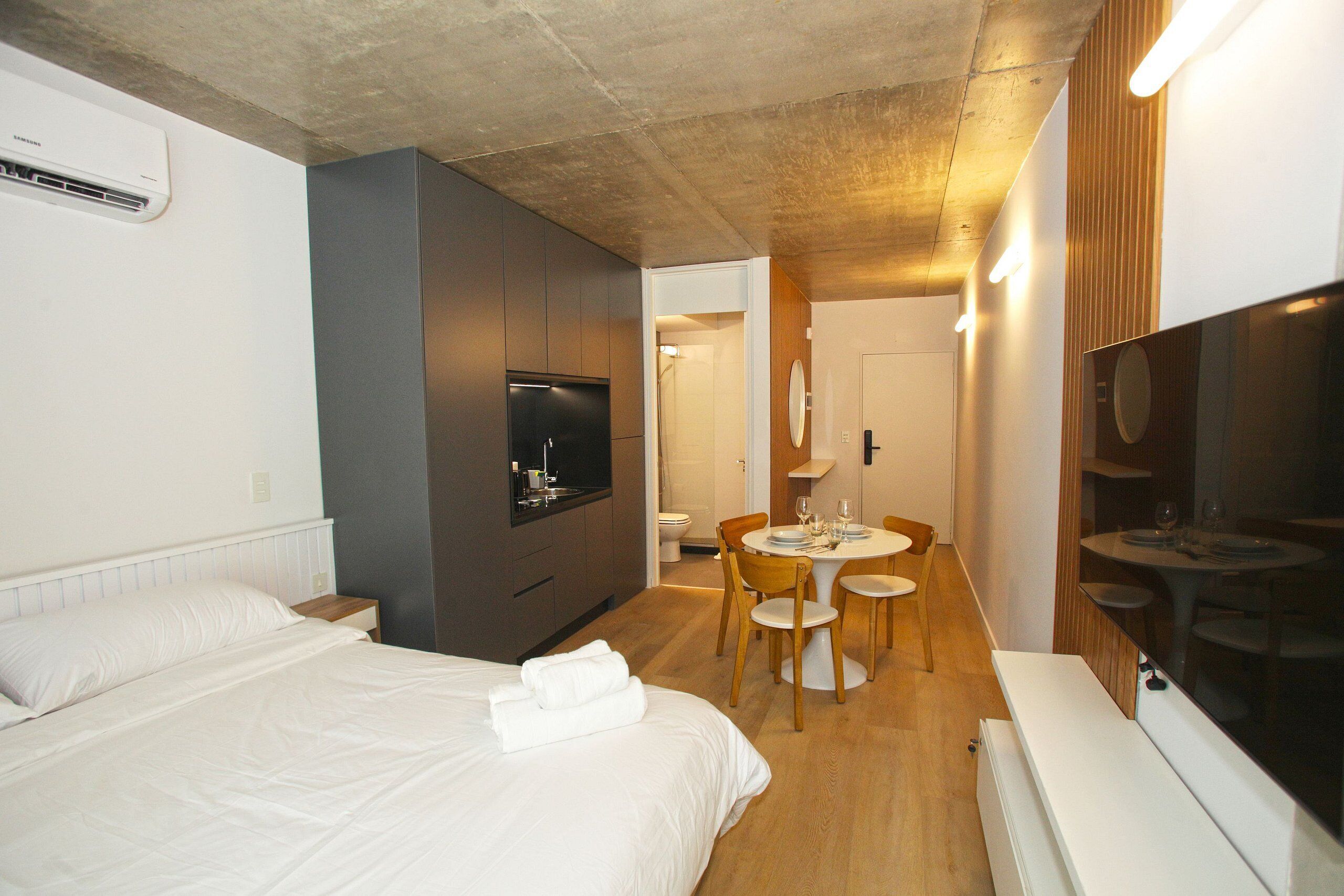 Una habitación de hotel con cama, televisor, mesa de comedor con sillas y una pequeña cocina.
