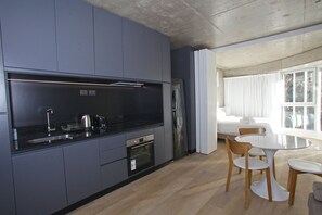 Una cocina moderna con armarios grises, un refrigerador de acero inoxidable y un horno empotrado. Hay un comedor con una mesa redonda y sillas de madera.