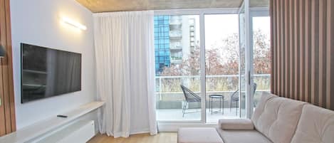 Een moderne woonkamer met een flatscreen televisie, een beige bank en een glazen schuifdeur naar een buitenbalkon.