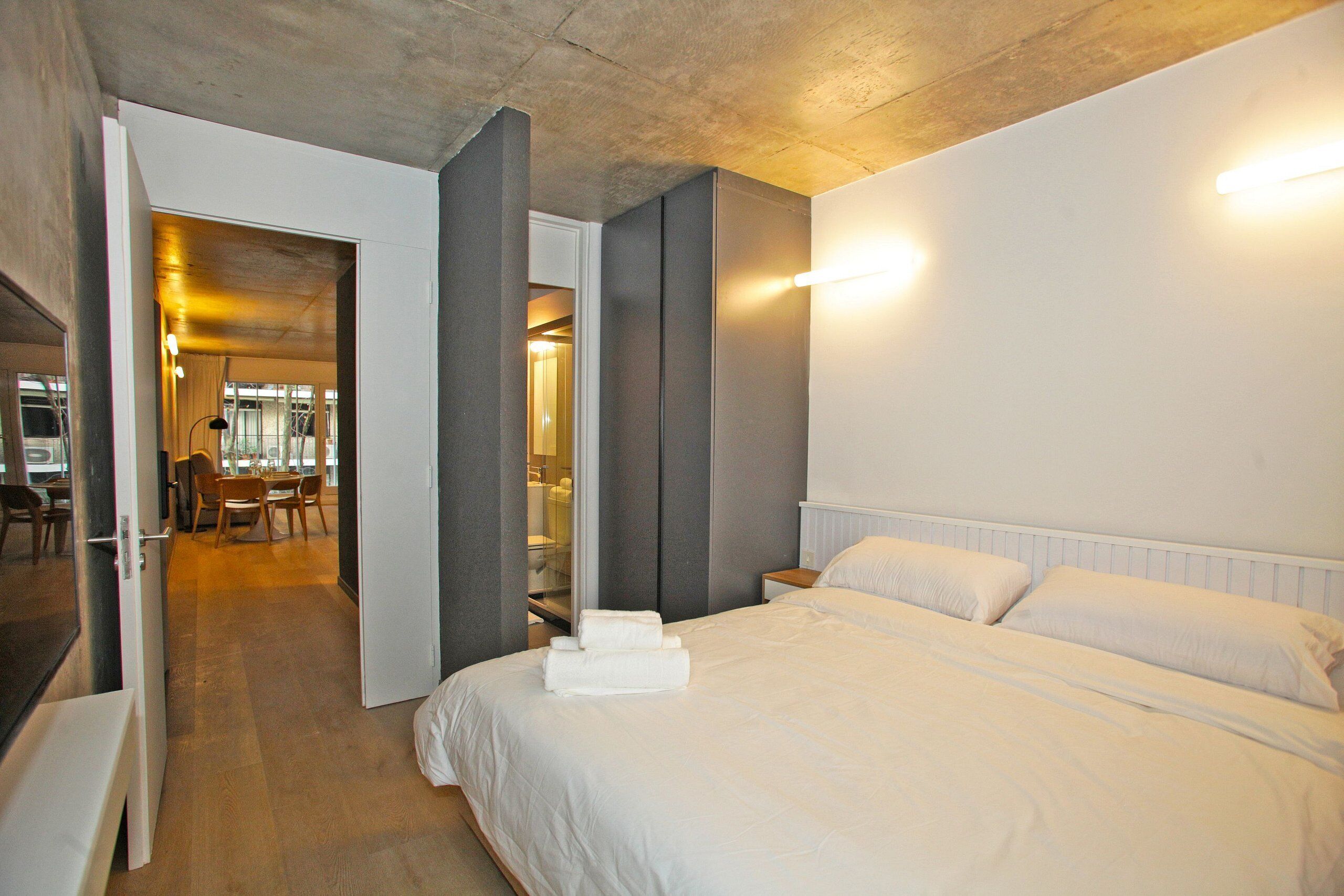 Una habitación de hotel con una cama grande, piso de madera y un área de comedor al fondo.