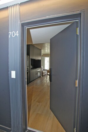 A modern interior with a dark door marked '704', leading to a kitchen area with wooden flooring and a visible dining area. - Urban Rent - Tu hogar temporario (Buenos Aires)