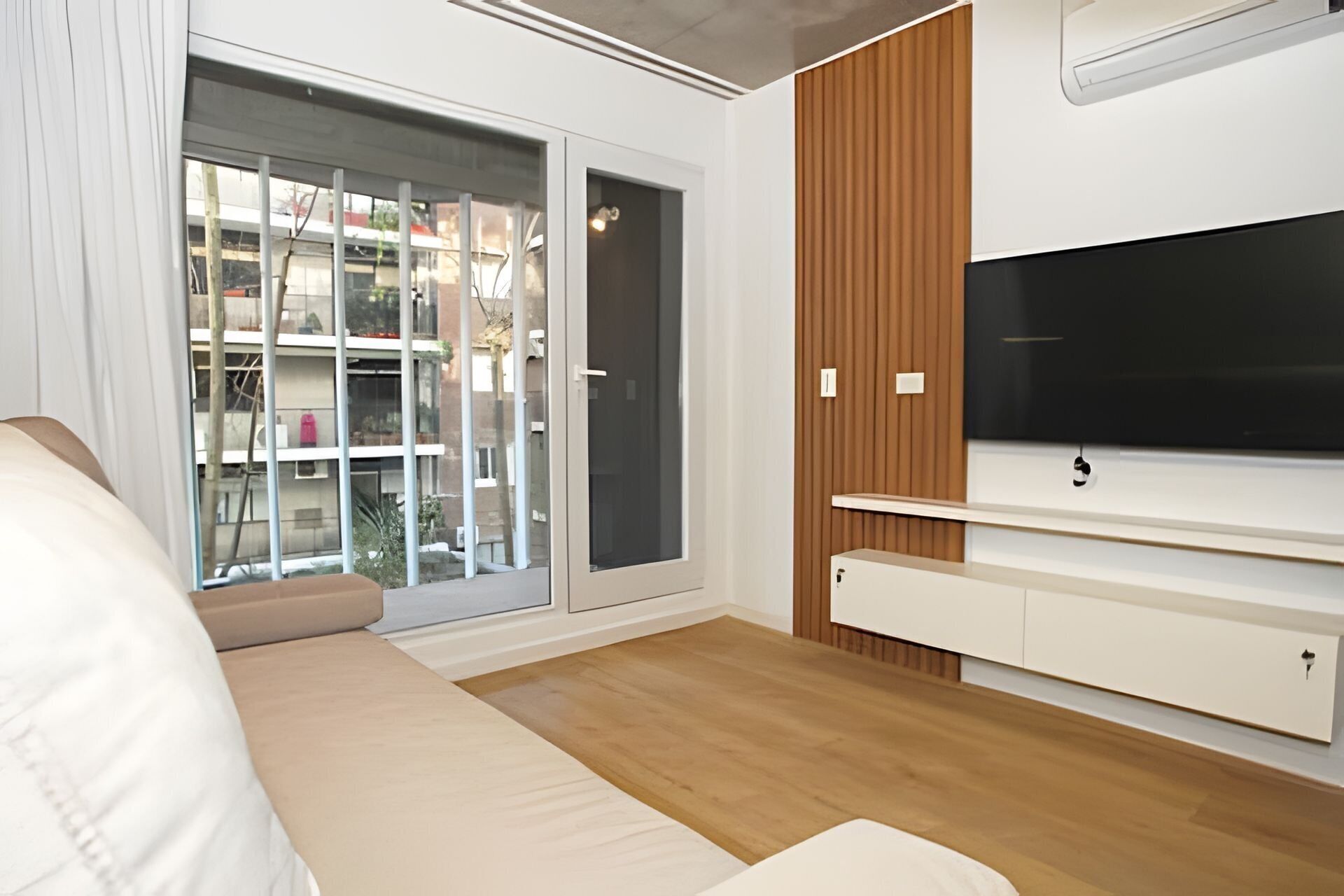 A modern living room with a large window, a flat-screen TV, and a sofa.