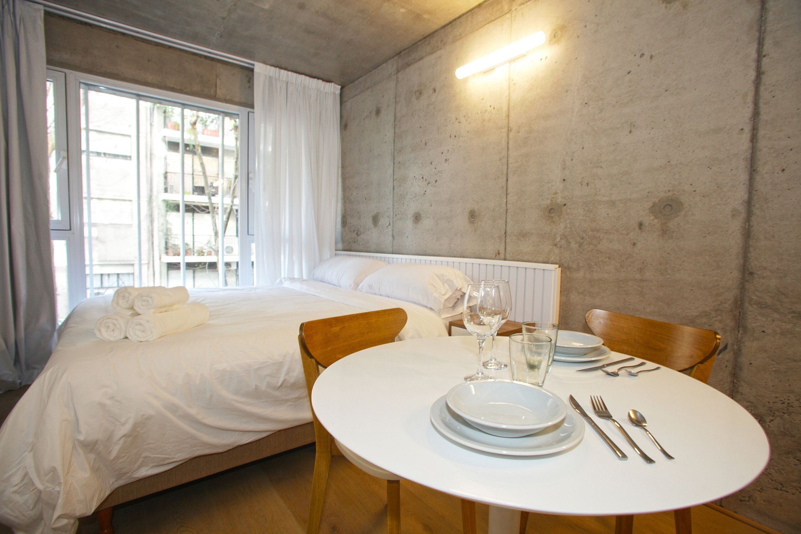 A hotel room with a bed, a round dining table with plates, cutlery, and a glass of water.