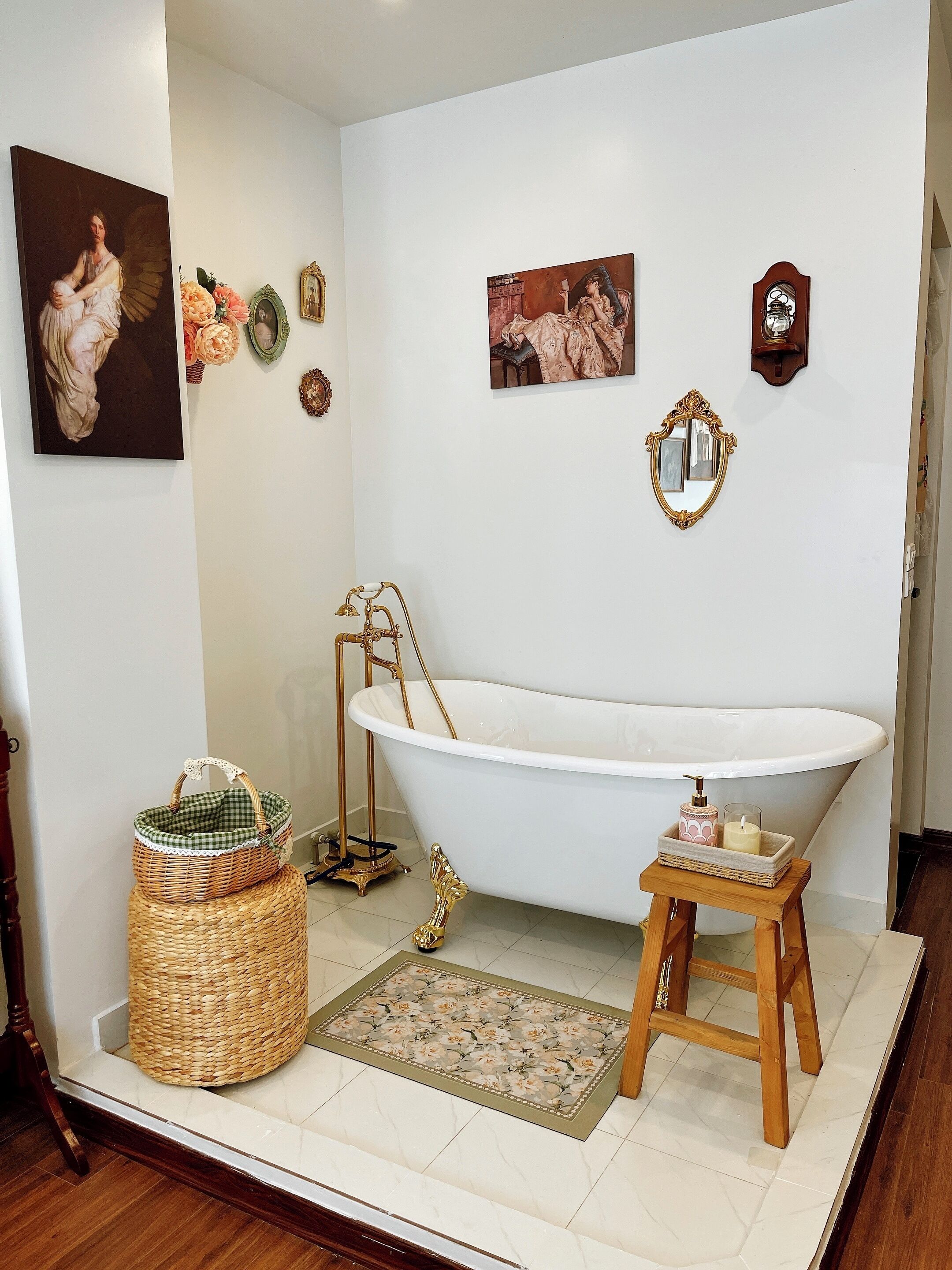 A bathroom with a freestanding bathtub, a wooden stool, a wicker basket, and decorative wall art.