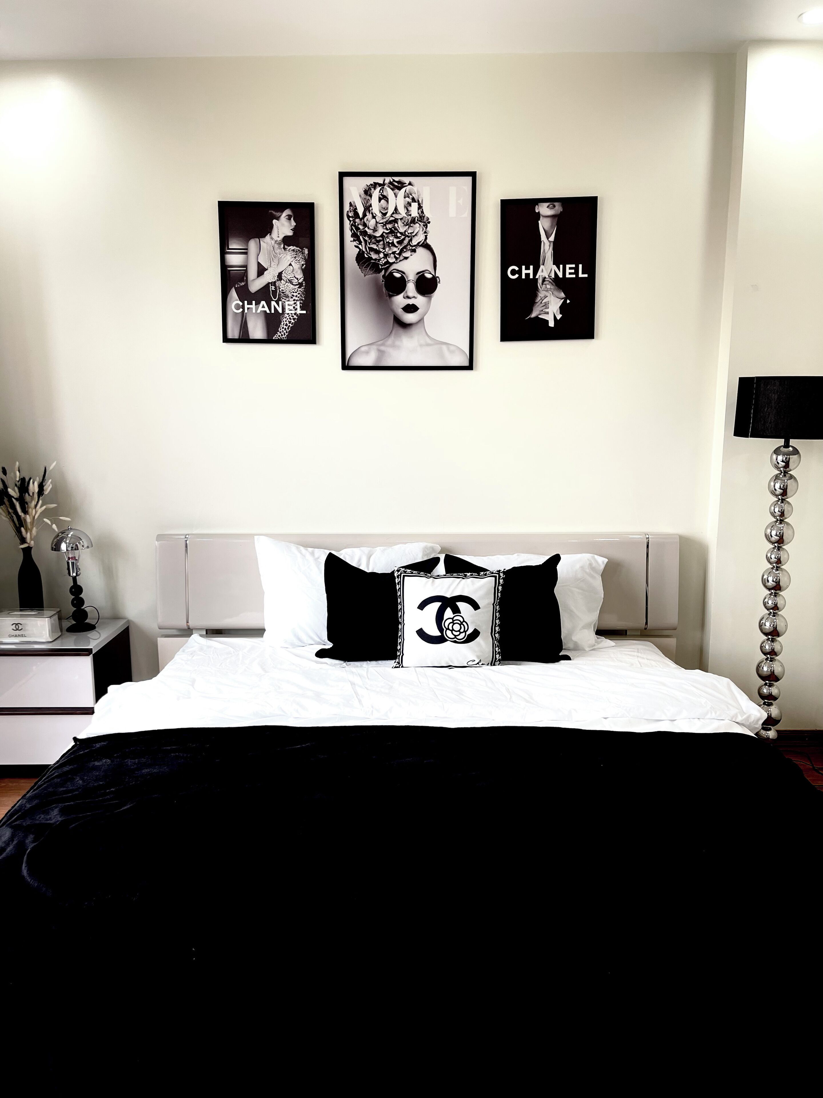 Un dormitorio con cama, una mesita de noche con lámpara y tres cuadros enmarcados en la pared.