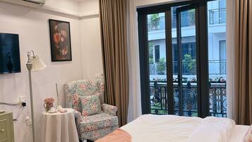 A hotel room with a large bed, a chair, a small table with a lamp, and a painting on the wall.