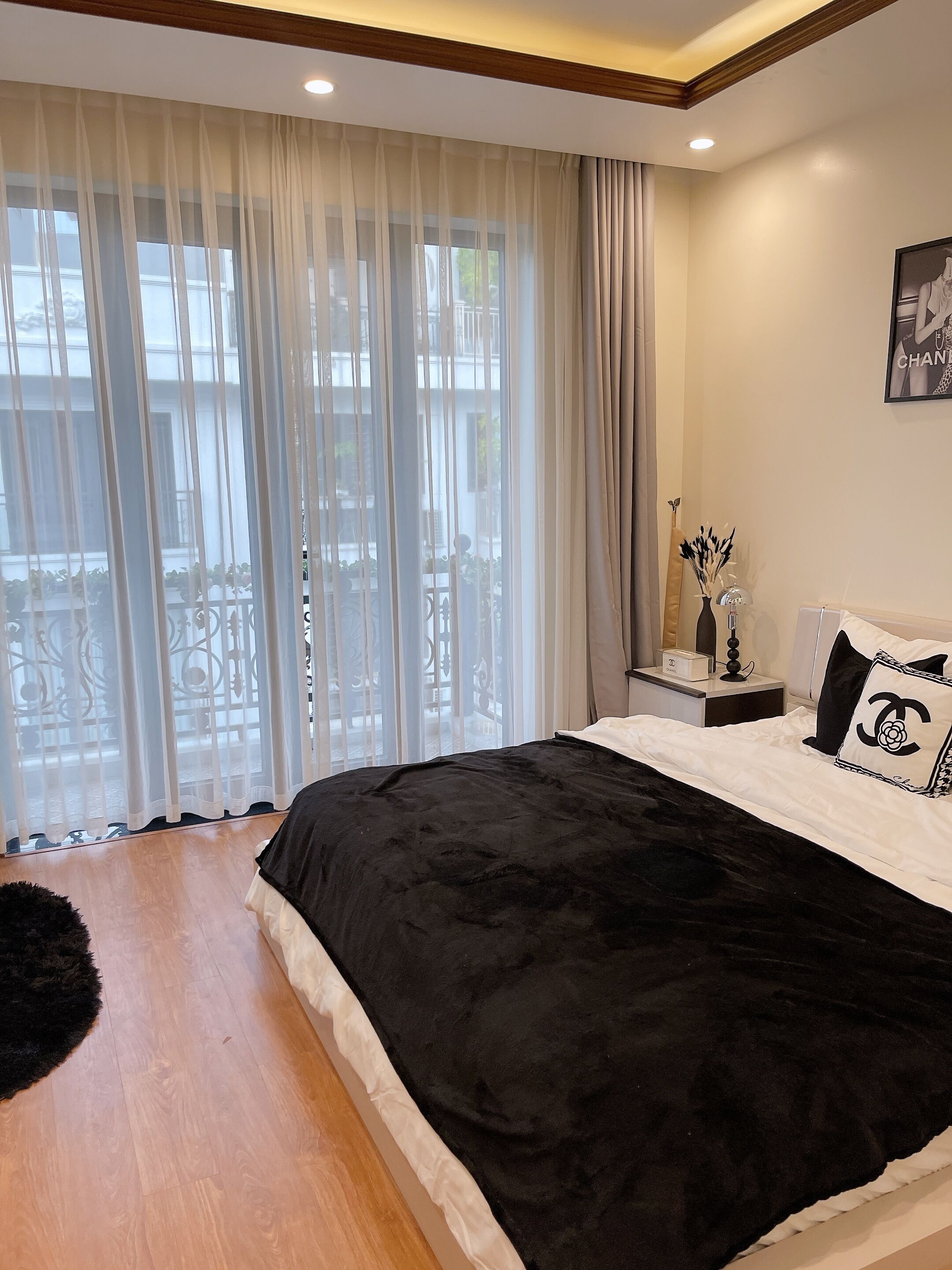 A bedroom with a large bed, a nightstand, a lamp, and a window with sheer curtains.