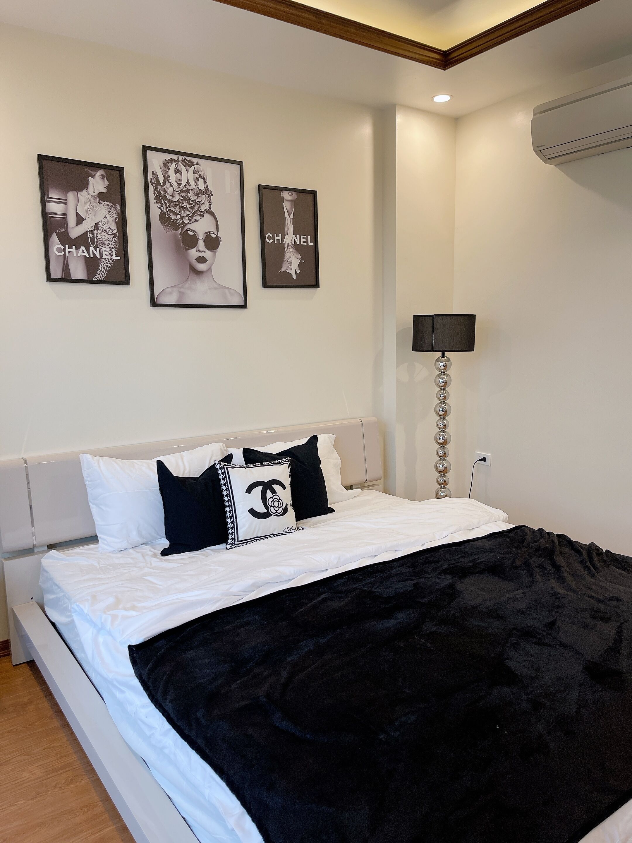 A bedroom with a bed, white bedding, a black blanket, and three framed pictures on the wall.