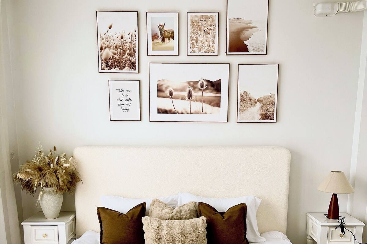 A neatly made bed with white linens and a woven throw blanket, a bedside table with a lamp, and a wall adorned with framed pictures.
