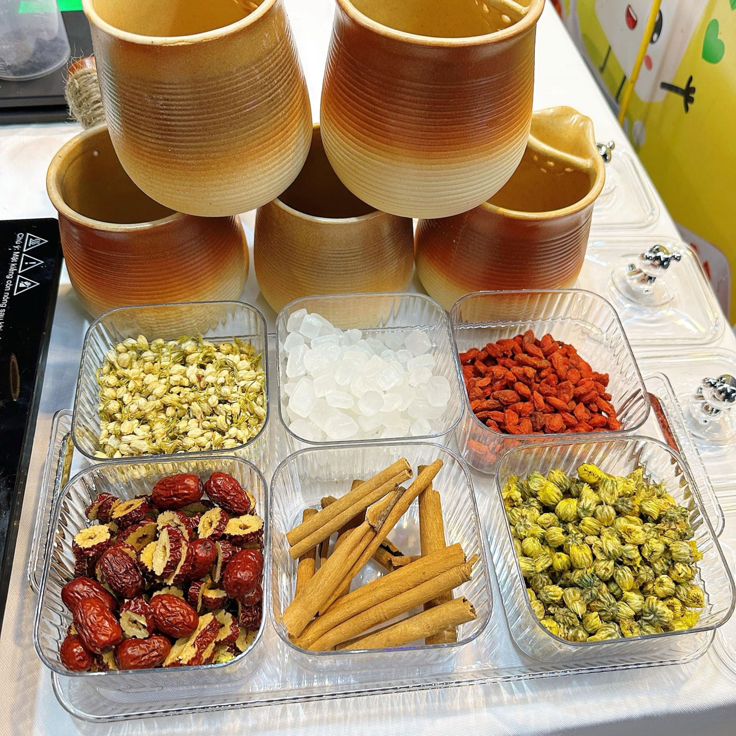 A table with various containers of snacks and a stack of ceramic cups.