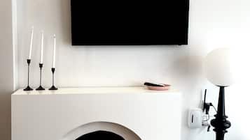 Een moderne kamer met een witte schoorsteen, een flatscreen televisie erboven en een zwarte vloerlamp naast de schoorsteen.