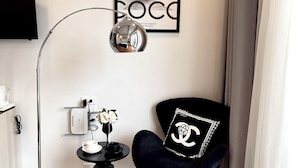 A modern room with a black floor lamp, a black chair with a Chanel logo, a framed artwork on the wall, and a small table with a vase of flowers. - C&K Luxury Homestay Hai Phong (Hai Phong)