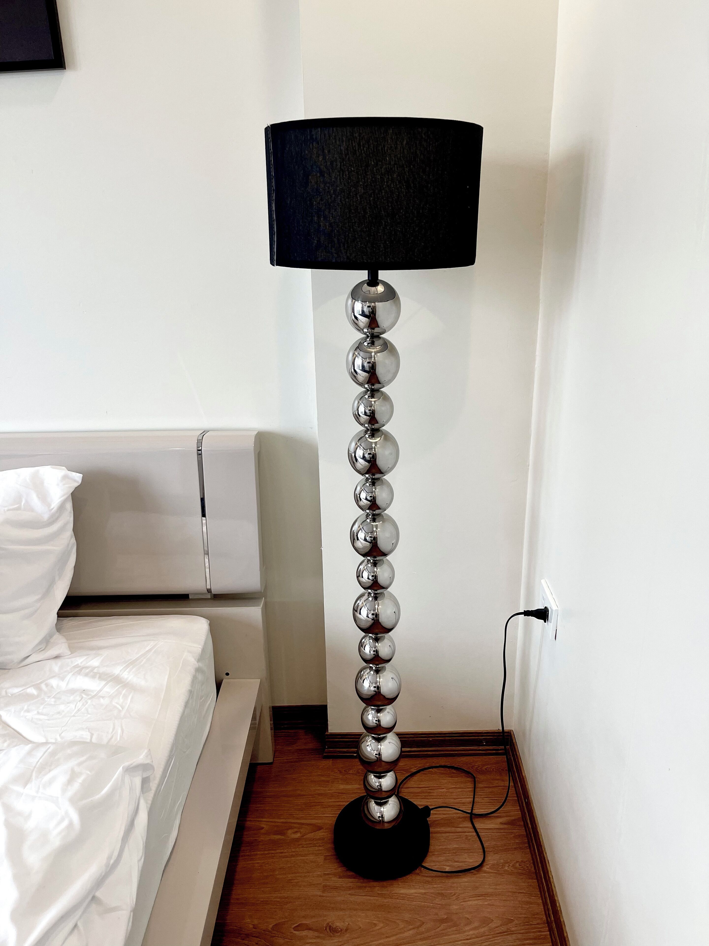 Ett modernt rum med en säng, en golvlampa med en svart lampskärm och ett trägolv.