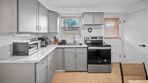 Een moderne keuken met grijze kastjes, een magnetron, een fornuis en een spoelbak.