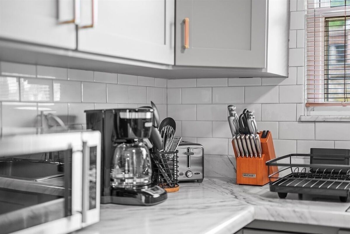 Une cuisine avec des meubles blancs, une machine à café, un grille-pain et un bloc à couteaux.