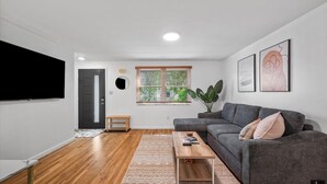 Een moderne woonkamer met een grijze bank, een salontafel en een aan de muur bevestigde televisie.