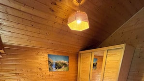 A wooden cabin bedroom with a bed, nightstands, a wardrobe, and a painting on the wall.