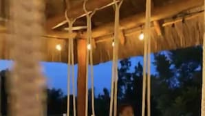 Eine Person schwingt sich unter einem reetgedeckten Bauwerk mit hängenden Lichtern.