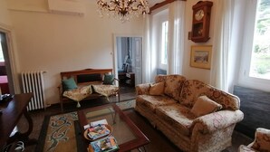 A living room with a sofa, a coffee table with magazines, a chandelier, a clock, and a view of the outdoors. - 3-bedroom condo, full kitchen, 1leaving room 1 bathroom, balcony great view (Camogli)