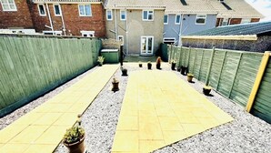 A residential area with a paved driveway, a green fence, and a row of houses in the background. - Stunning Double Bedroom House Closer to the sea (Hartlepool)