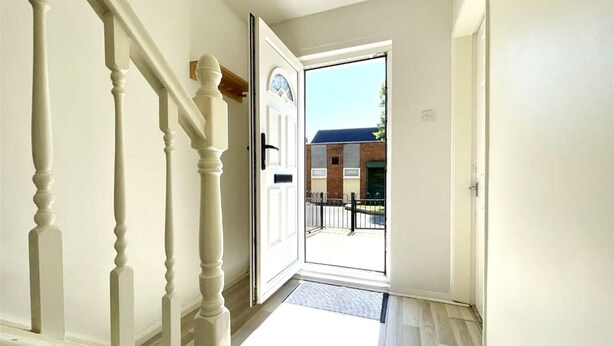 A hallway with a white door leading outside, a wooden staircase, and a view of a brick building through the door. - Stunning Double Bedroom House Closer to the sea (Hartlepool)