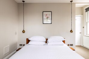 A neatly made bed with white linens, a framed picture of a flamingo on the wall, and a door to the right. - Rustic and Contemporary Haven in Brixton (London)