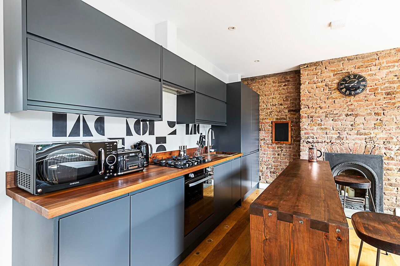 A modern kitchen with a wooden bar, built-in appliances, and a brick wall.