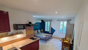 A compact kitchen with a microwave, a bed with a colorful headboard, and a dining area with a table and chairs. - Studio Van Gogh - Air conditionning (Arles)