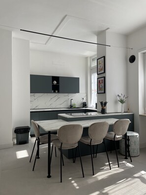 A modern kitchen with a marble countertop, a built-in island with seating, and a dining area with chairs. - Casa Viola by Wonderful Italy (Turin)