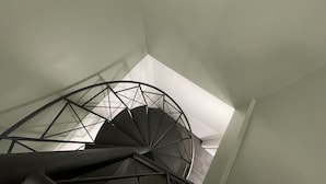 Una escalera en espiral con barandilla metálica geométrica y pared blanca.