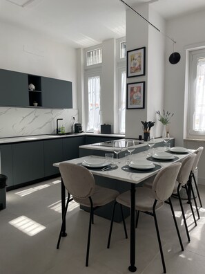 A modern kitchen with a marble backsplash, grey cabinets, and a dining area set for six with white chairs and a marble table. - Casa Viola by Wonderful Italy (Turin)