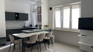 Una cocina moderna con una isla central, sillas de comedor, un televisor y una ventana con persianas.