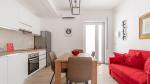 A modern kitchen with white cabinets, a wooden dining table, and a red couch.