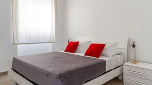 A bedroom with a bed, white nightstand, and a bedside table with a lamp.