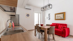 A modern kitchen with a sink, a dining table with chairs, and a red sofa in the living area.