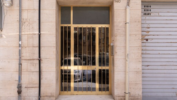 A building entrance with a metal gate, a number "140" above the door, and a garage door to the right.