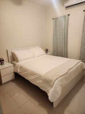 Quarto com cama, mesas de cabeceira, abajur e ar condicionado.