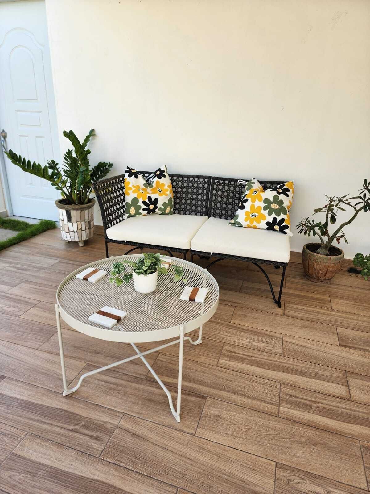 Un sofá blanco con cojines estampados, una mesa redonda de metal con cojín blanco y plantas en macetas.