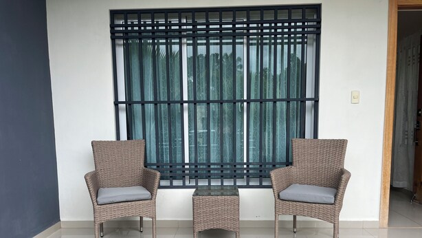 A room with two wicker chairs, a small table, and a large window with a metal grille.