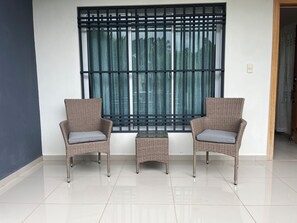 Ein Zimmer mit zwei Korbstühlen, einem kleinen Tisch und einem großen Fenster mit Metallgitter.