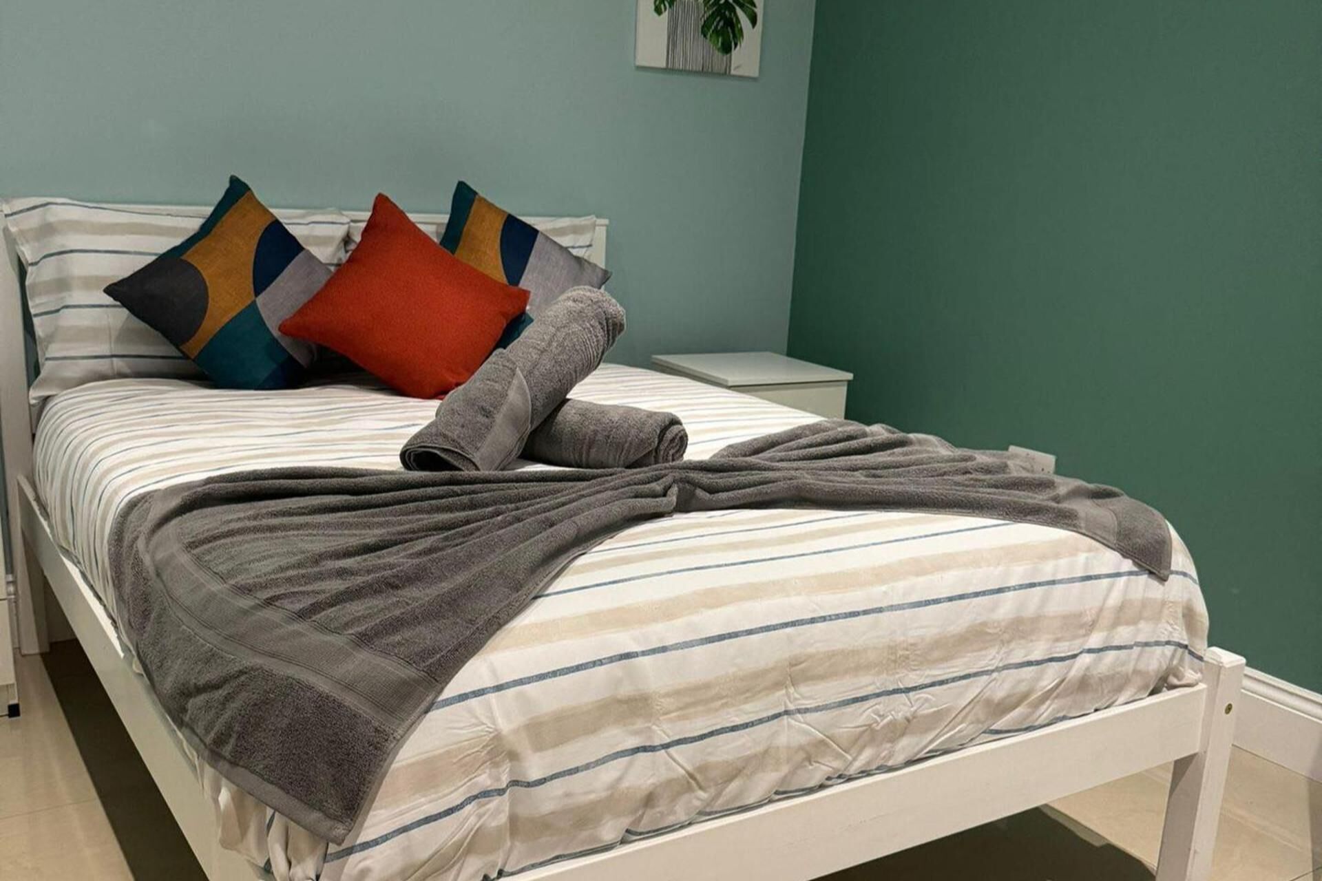 A bed with striped bedding, a gray blanket, and colorful pillows.
