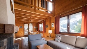 A cozy wooden cabin interior with a stone fireplace, a sofa, a table, and a dining area.