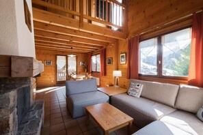 Ein gemütliches Holzhaus-Interieur mit Kamin aus Stein, einer Couch, einem Tisch und einem Essbereich.