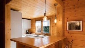 A wooden cabin interior with a kitchen area featuring a wooden countertop, a sink, and pendant lighting.