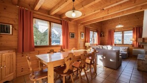 A wooden cabin interior with a dining table, chairs, a sofa, and a fireplace.